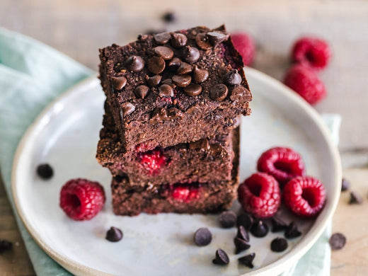 A stack of three brownies surrounded by raspberries and chocolate chips